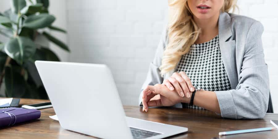 mulher em escrítorio em frente ao notebook olhando para relógio pensando na gestão de pontos