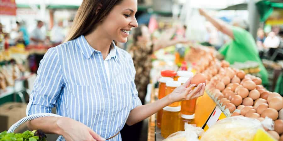 mulher branca segurando ovo em supermercado pensando o que pode comprar com o vale-alimentação