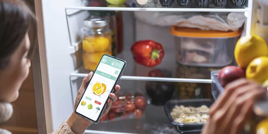trabalhadora utilizando um aplicativo de alimentação em frente a uma geladeira