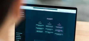 A imagem mostra a parte de trás da cabeça e os ombros de uma pessoa (provavelmente um homem, dado o corte de cabelo curto) sentada de costas para o observador, usando um laptop.