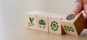 Mão colocando um bloco com "ESG" em uma série de blocos de madeira representando ícones de sustentabilidade, responsabilidade social e governança.