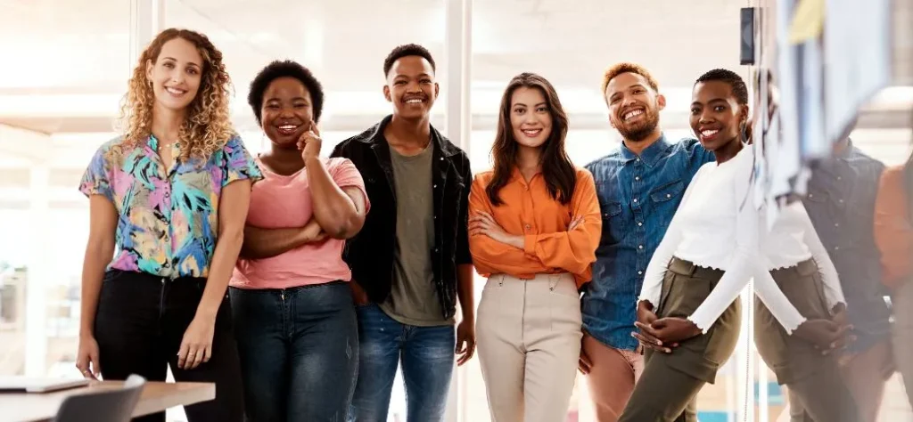 Um grupo diversificado de seis pessoas está reunido em um espaço de escritório moderno, apresentando uma fachada unida, com luz natural iluminando o cenário.