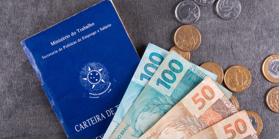 carteira de trabalho e cedulas de reais em cima da mesa representando salário mínimo em 2022