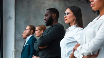 Um grupo de indivíduos vestidos profissionalmente estão juntos, exibindo uma mistura de trajes formais, em um ambiente de escritório moderno.