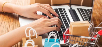 Comprador online aproveitando promoções: mãos digitando em laptop com sacolas e caixas ao redor, simbolizando a finalização de um pedido.
