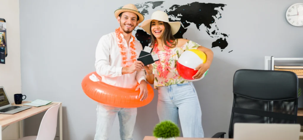 Um casal sorridente em escritório, ele com boia e ela com bola de praia. Têm passagens e chapéus. Mapa-múndi na parede.