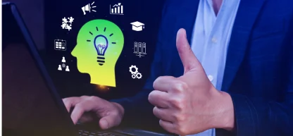 A imagem mostra uma pessoa de terno, com a mão esquerda no teclado de um notebook e a mão direita levantada, fazendo um sinal de "joinha" com o polegar. A mão direita e parte do braço estão em foco, e a pessoa está de frente para o notebook, que está à esquerda da imagem.