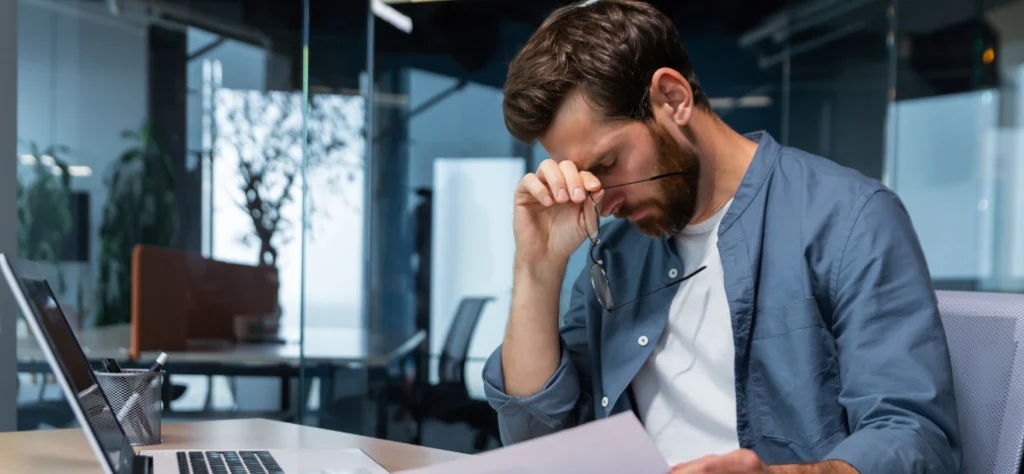Funcionário estressado lendo um papel na mesa do escritório, relacionado a demissão, aviso prévio ou contrato. (