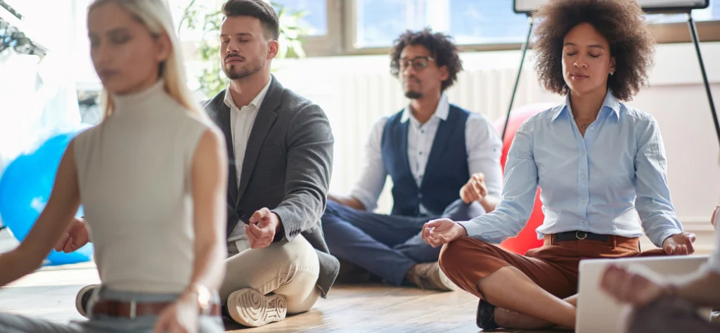 Grupo de colegas de trabalho sentados em posição de lótus, meditando com os olhos fechados em um escritório