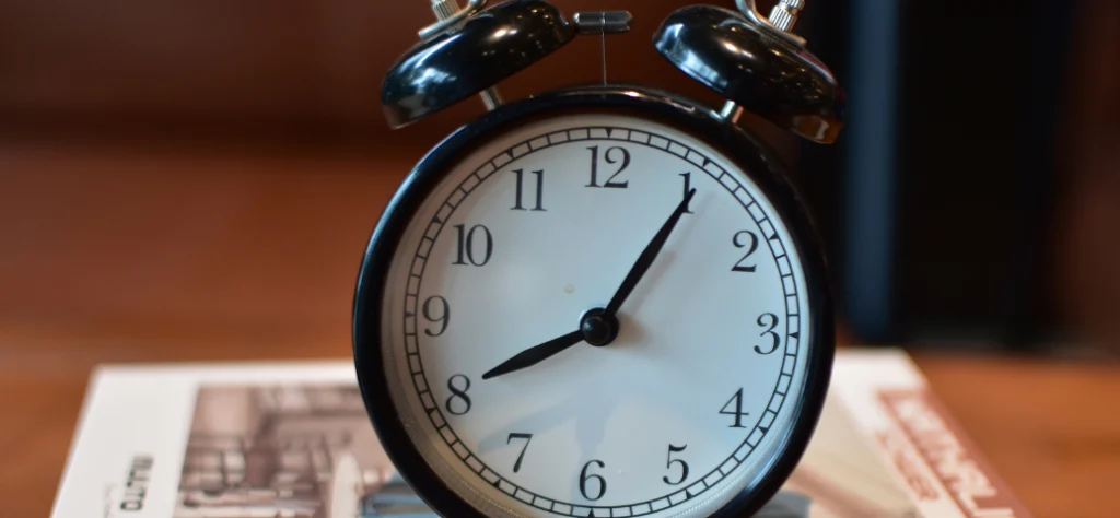 Relógio despertador vintage preto e branco marcando aproximadamente 8h05, representando o tempo de trabalho ou feriado.