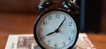 Relógio despertador vintage preto e branco marcando aproximadamente 8h05, representando o tempo de trabalho ou feriado.