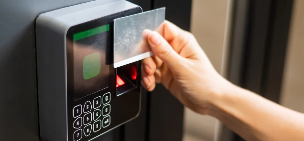 Mão passando um cartão (crachá) em um relógio de ponto eletrônico ou sistema de controle de acesso biométrico.