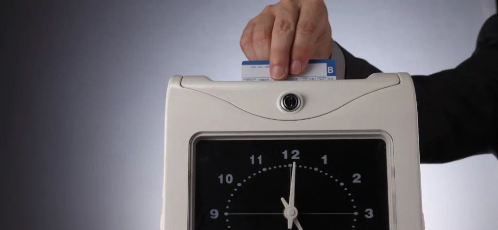 Mão inserindo um cartão de ponto cartográfico (ponto manual) em um relógio de ponto mecânico antigo