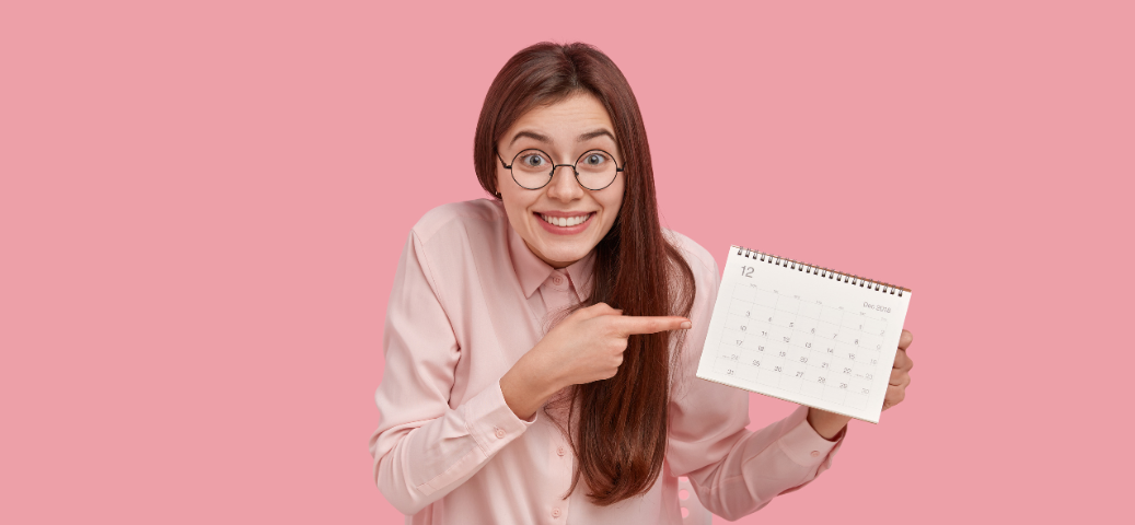 Mulher sorridente de óculos apontando para um calendário, representando feriados e folgas.