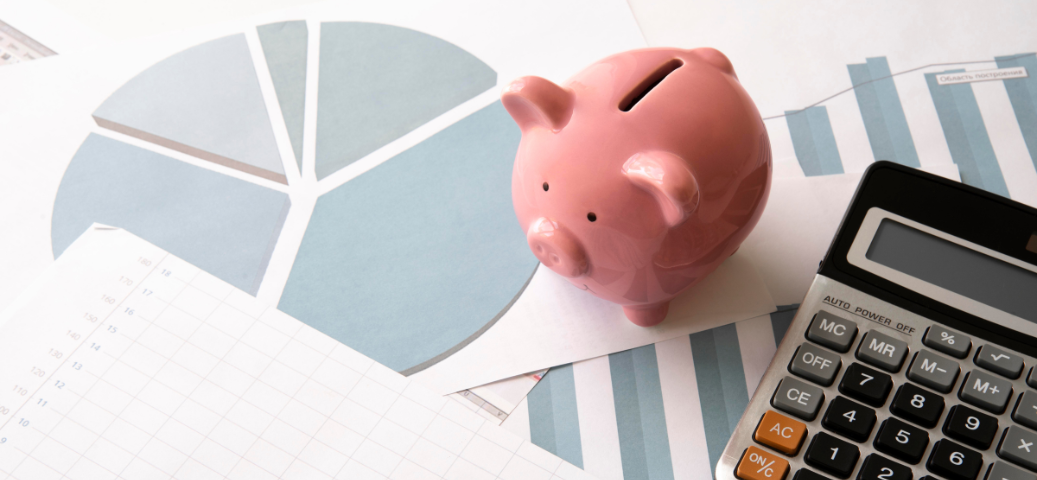 Porquinho rosa, calculadora e gráficos de pizza sobre a mesa, simbolizando planejamento financeiro empresarial