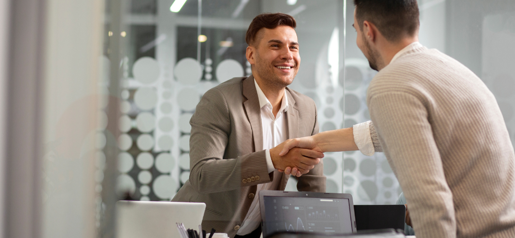 Dois homens de negócios sorridentes apertam as mãos em um escritório moderno, simbolizando parceria e acordo profissional.