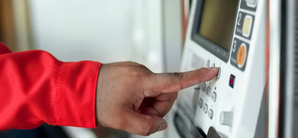 Close-up de uma mão de camisa vermelha pressionando um botão em um painel de controle ou máquina de ponto. Registro manual.