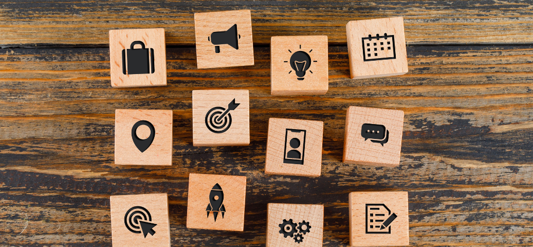 Blocos de madeira com ícones de negócios e marketing, como maleta, megafone, lâmpada, calendário, alvo, foguete, e engrenagens.