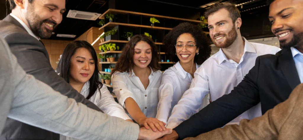 Grupo de profissionais diversos sorrindo e unindo as mãos no centro, simbolizando união e cultura organizacional.