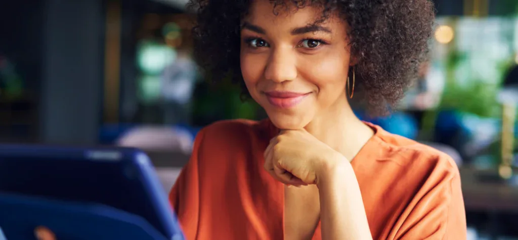 Uma profissional de saúde sorri ao usar um tablet em um ambiente moderno, representando inovação e agilidade no trabalho.