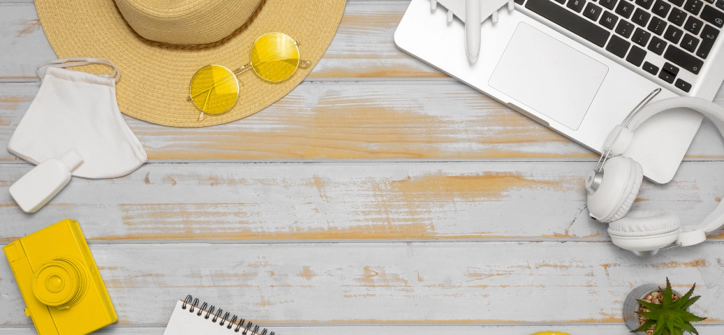 Gemini said Vista superior de mesa de madeira com chapéu, óculos escuros, câmera amarela, notebook, fones de ouvido e máscara branca.