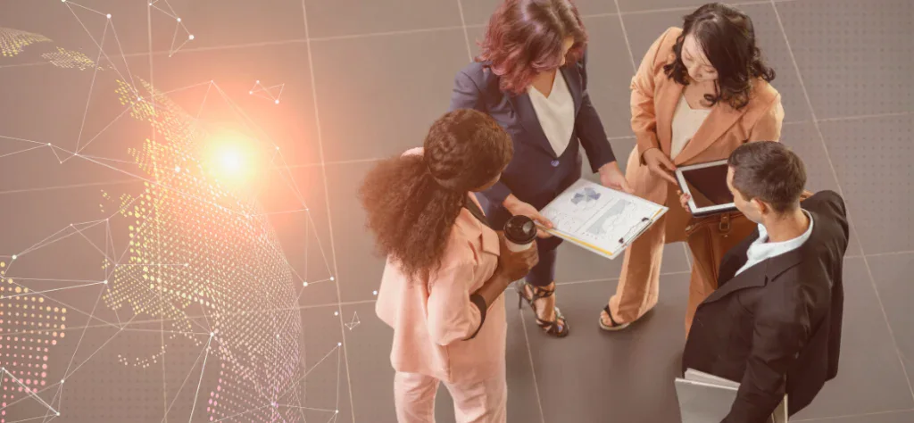Vista superior de quatro profissionais em círculo analisando gráficos em uma prancheta e um tablet. Conectividade global.