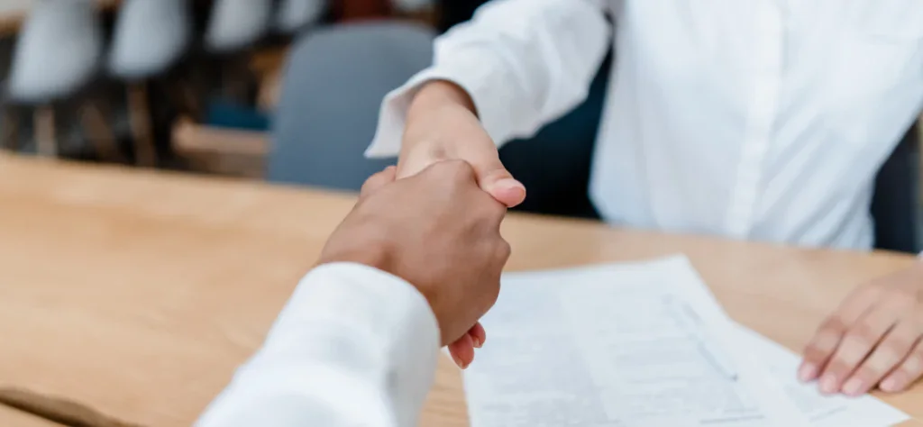 O Gemini disse Aperto de mãos sobre um contrato em uma mesa de madeira, simbolizando a conclusão de um acordo ou nova contratação.