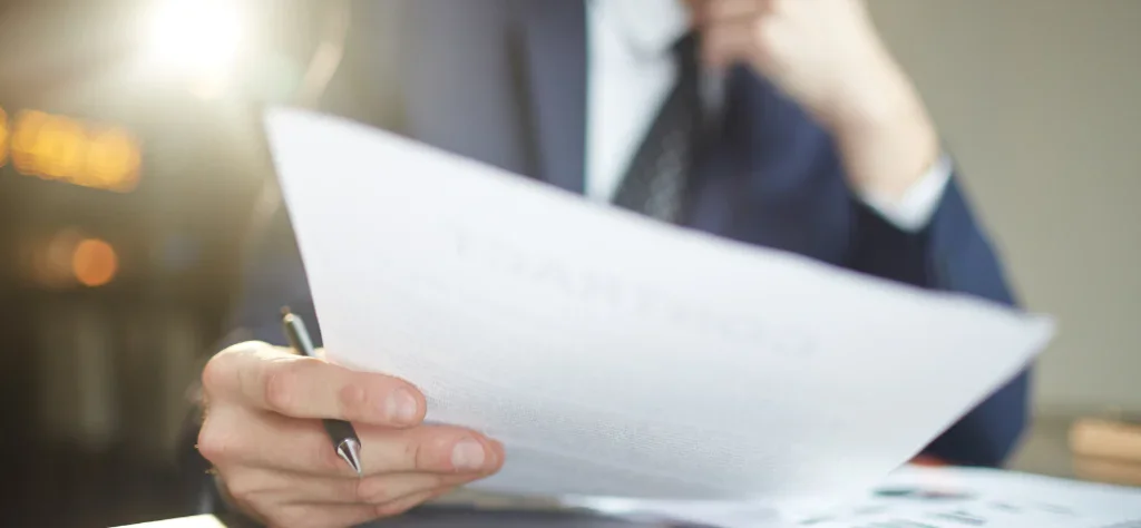 Homem em traje social analisa atentamente um documento de rescisão contratual, com foco nas mãos e no papel em ambiente iluminado.