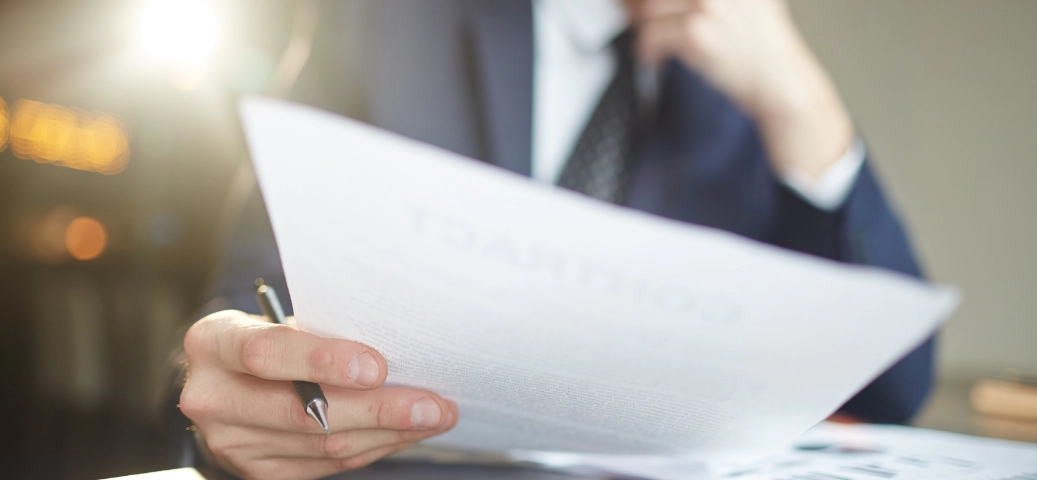 Homem em traje social analisa atentamente um documento de rescisão contratual, com foco nas mãos e no papel em ambiente iluminado.