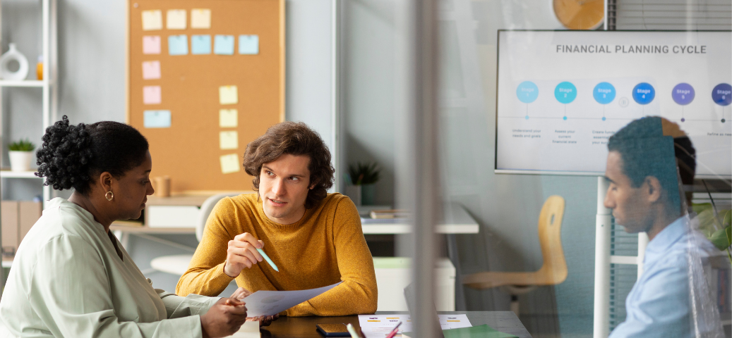 Equipe em reunião discute ciclo de planejamento, com gráficos em tela e anotações, focando em metas e estratégias.