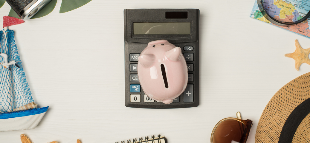 Porquinho de plástico sobre calculadora, rodeado por itens de viagem como mapa e chapéu, simbolizando economia para férias.