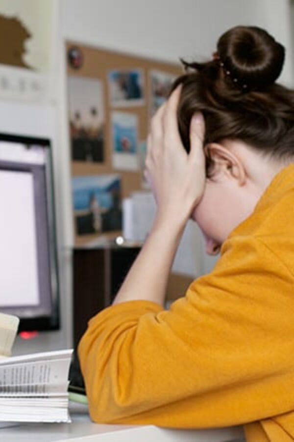 mulher representando o que é sindrome de burnout sentada em frente ao computador com a mão na cabeça