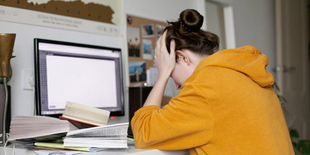 mulher representando o que é sindrome de burnout sentada em frente ao computador com a mão na cabeça