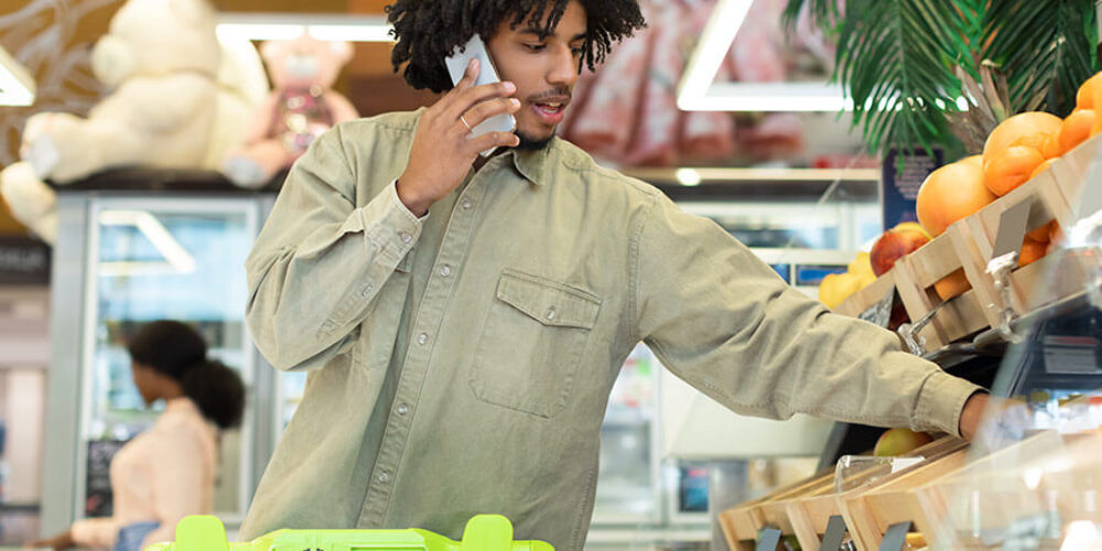 homem no supermercado falando no celular perguntando o que não pode comprar com vale-alimentação